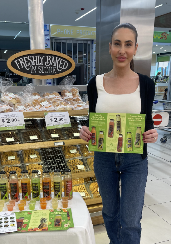 Rachael presenting juices beside a freshly baked in store display